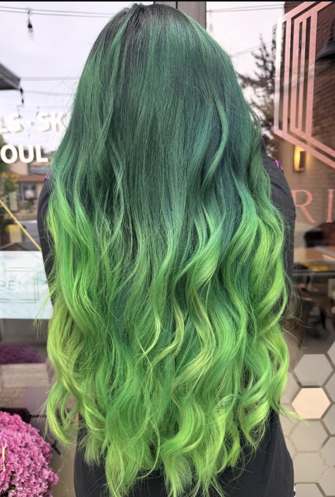 Back view of a person with long, wavy hair dyed in shades of green, from dark to bright lime green.