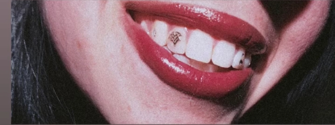 Close-up of a person's smiling mouth with red lipstick, showing teeth and a pierced lip.