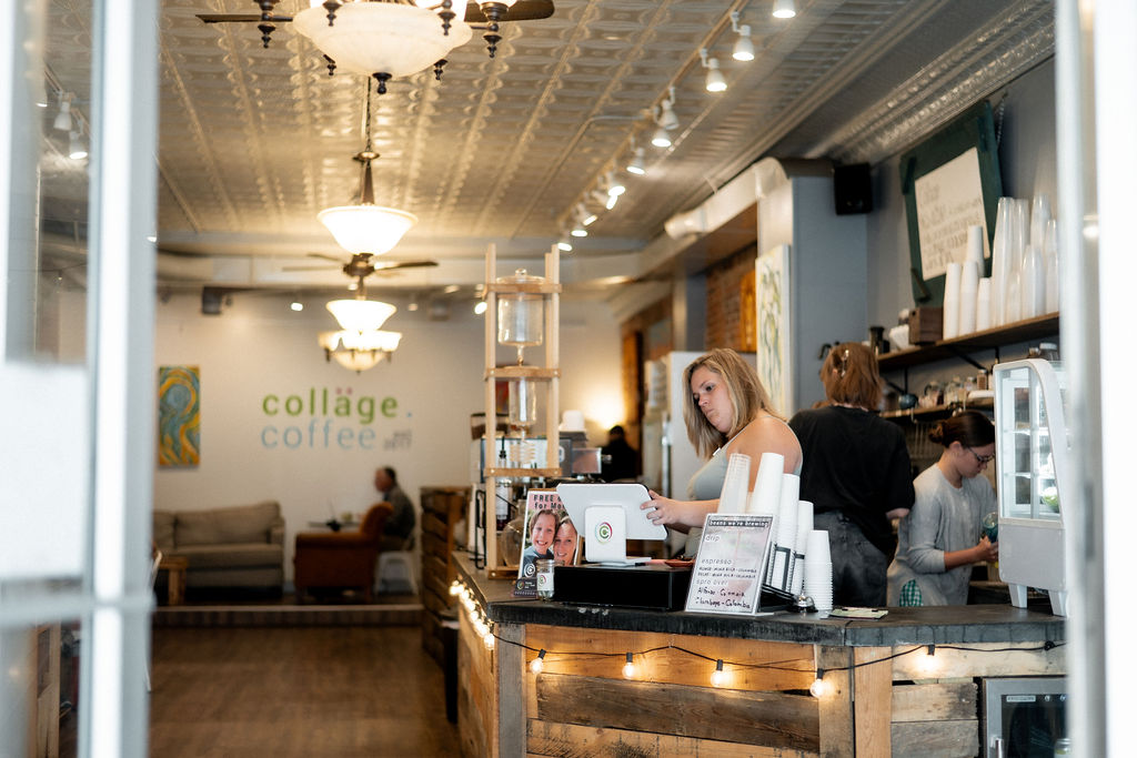 Coffee shop interior with a counter, barista, and customers, decorated with chandeliers and artwork on the walls.
