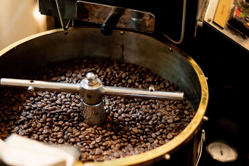 Coffee beans in a roasting machine with a metal arm stirring them, inside a round metal drum.