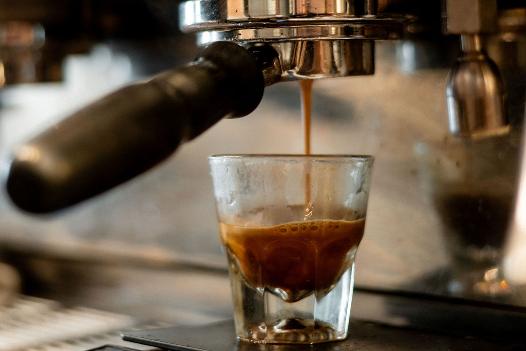 Espresso shot being poured into a glass from a coffee machine spout, with a dark coffee stream and a glass below.