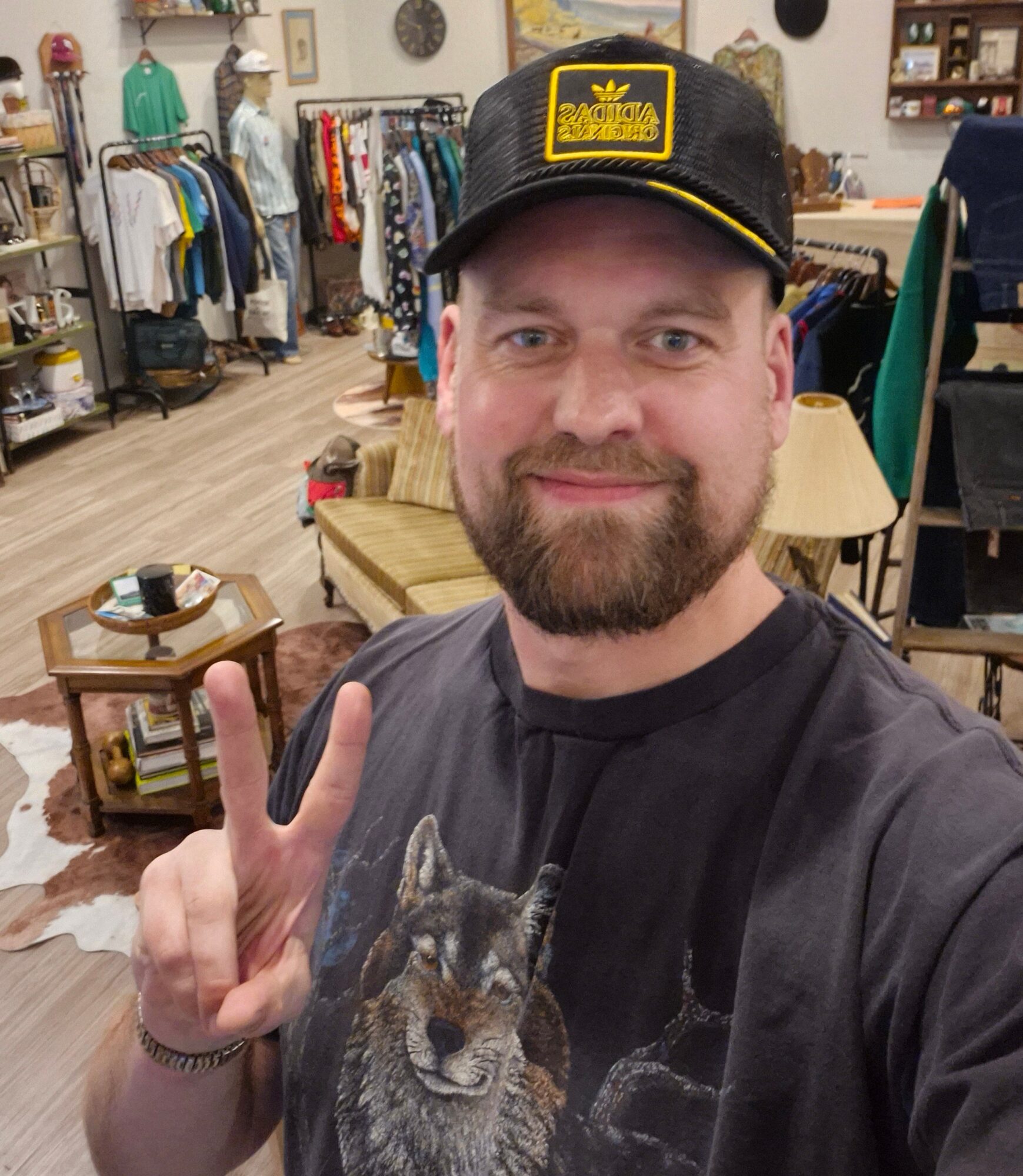 Man with beard wearing a black cap and black T-shirt making a peace sign in a clothing store.
