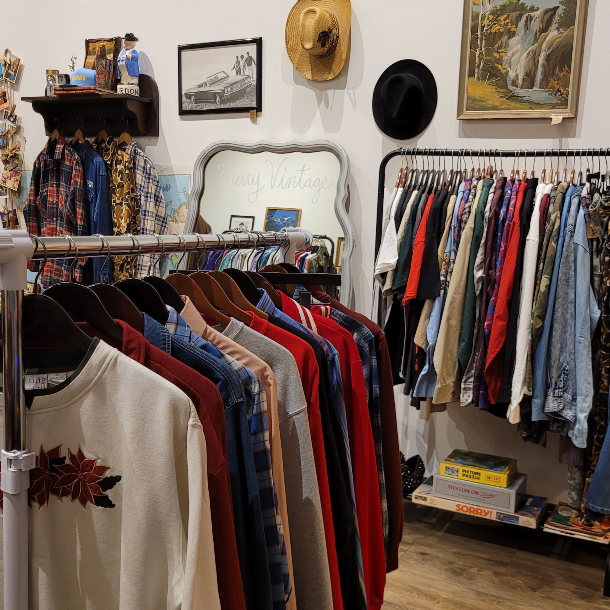 Clothing rack with various shirts and garments, shelves with folded clothes, framed pictures, and decorative items on the wall.