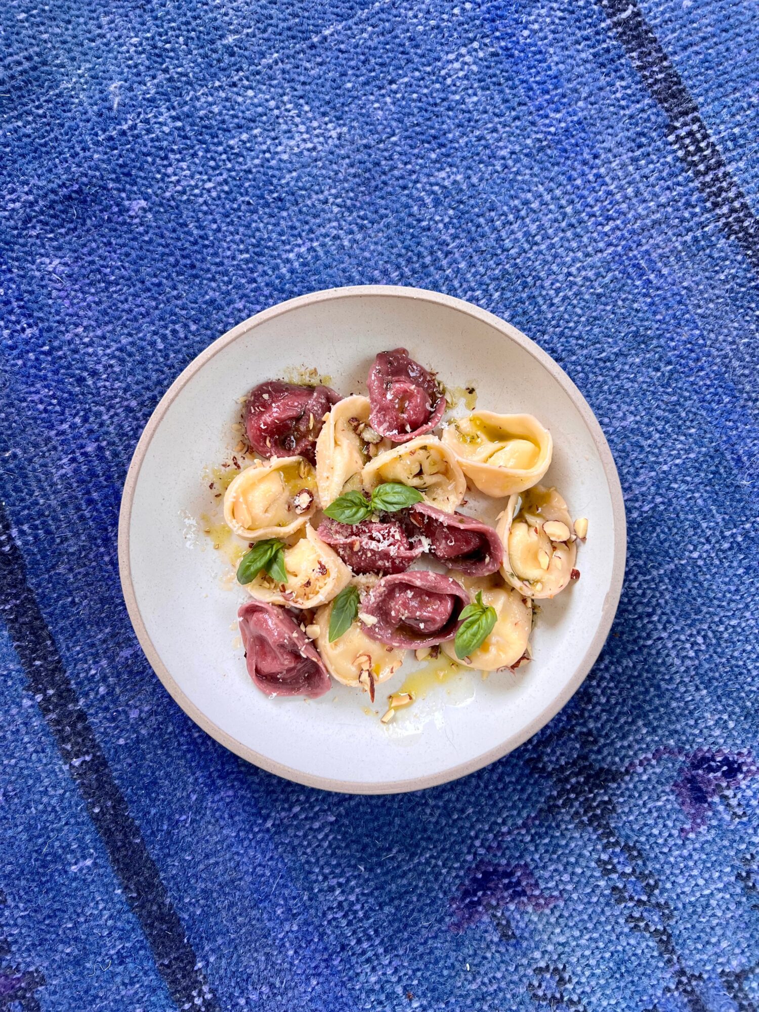 Plate of raw beef, pasta, and basil on a blue textured surface.