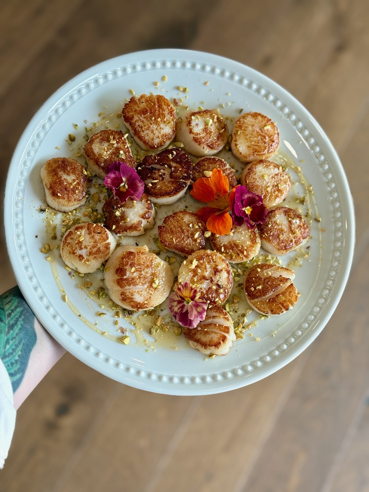 Plate with small round desserts garnished with edible flowers and crumbs, on a wooden surface.