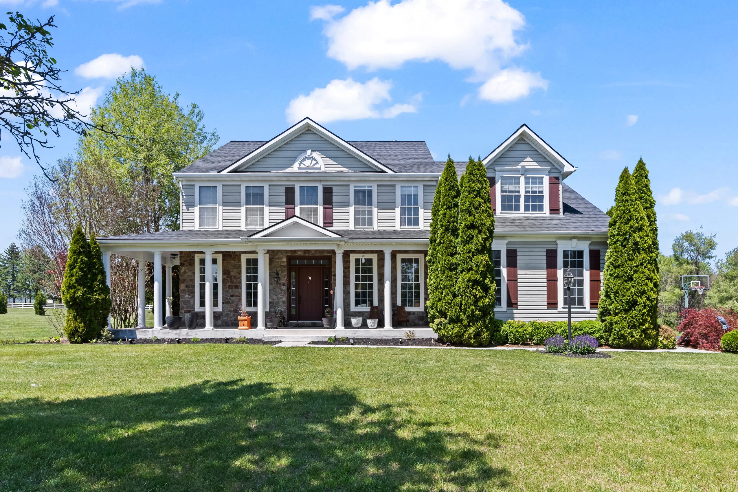 Large house with a front porch, multiple windows, and a well-maintained lawn, under a blue sky with clouds.