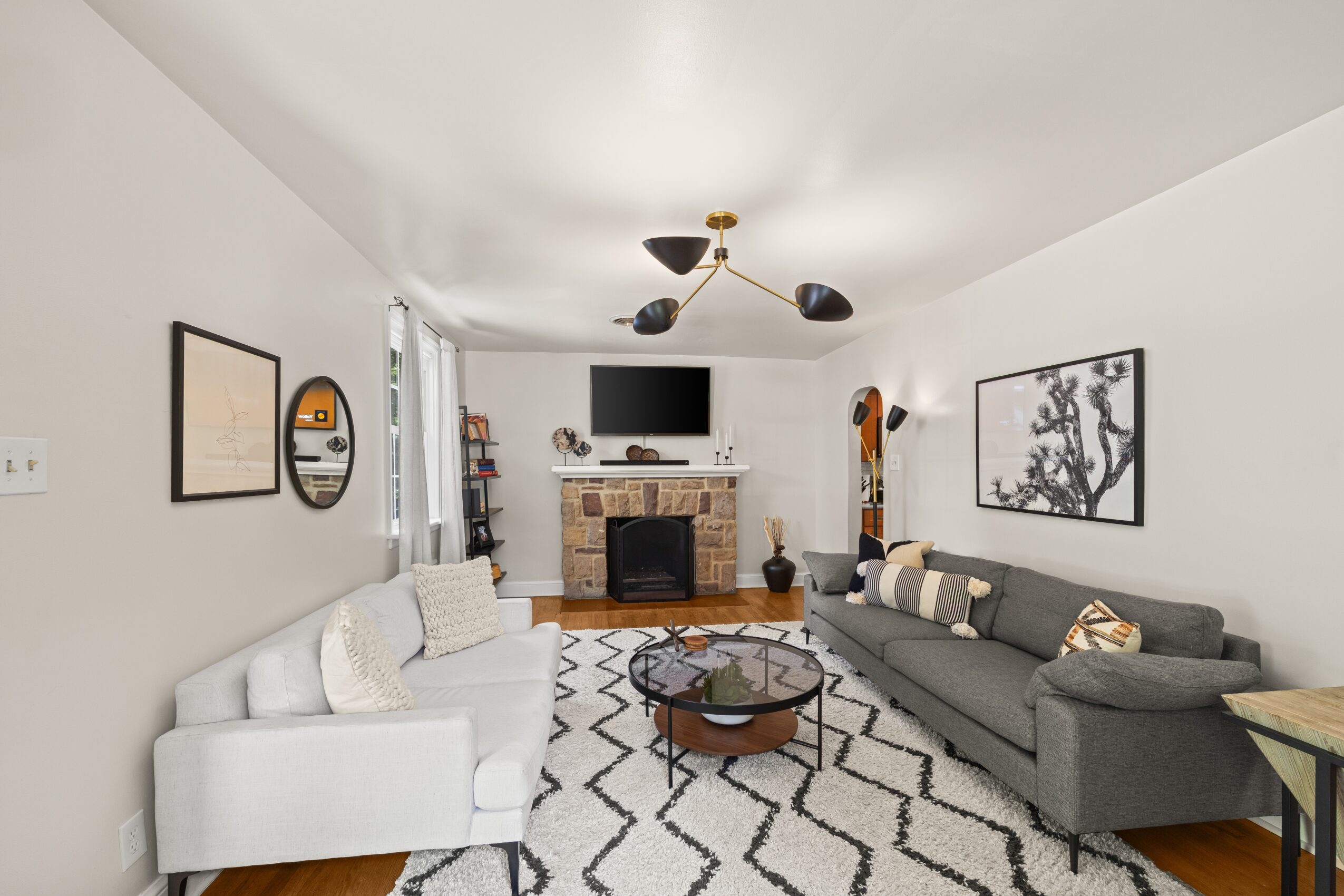 Living room with white and gray sofas, a brick fireplace, a wall-mounted TV, and black and white wall art.