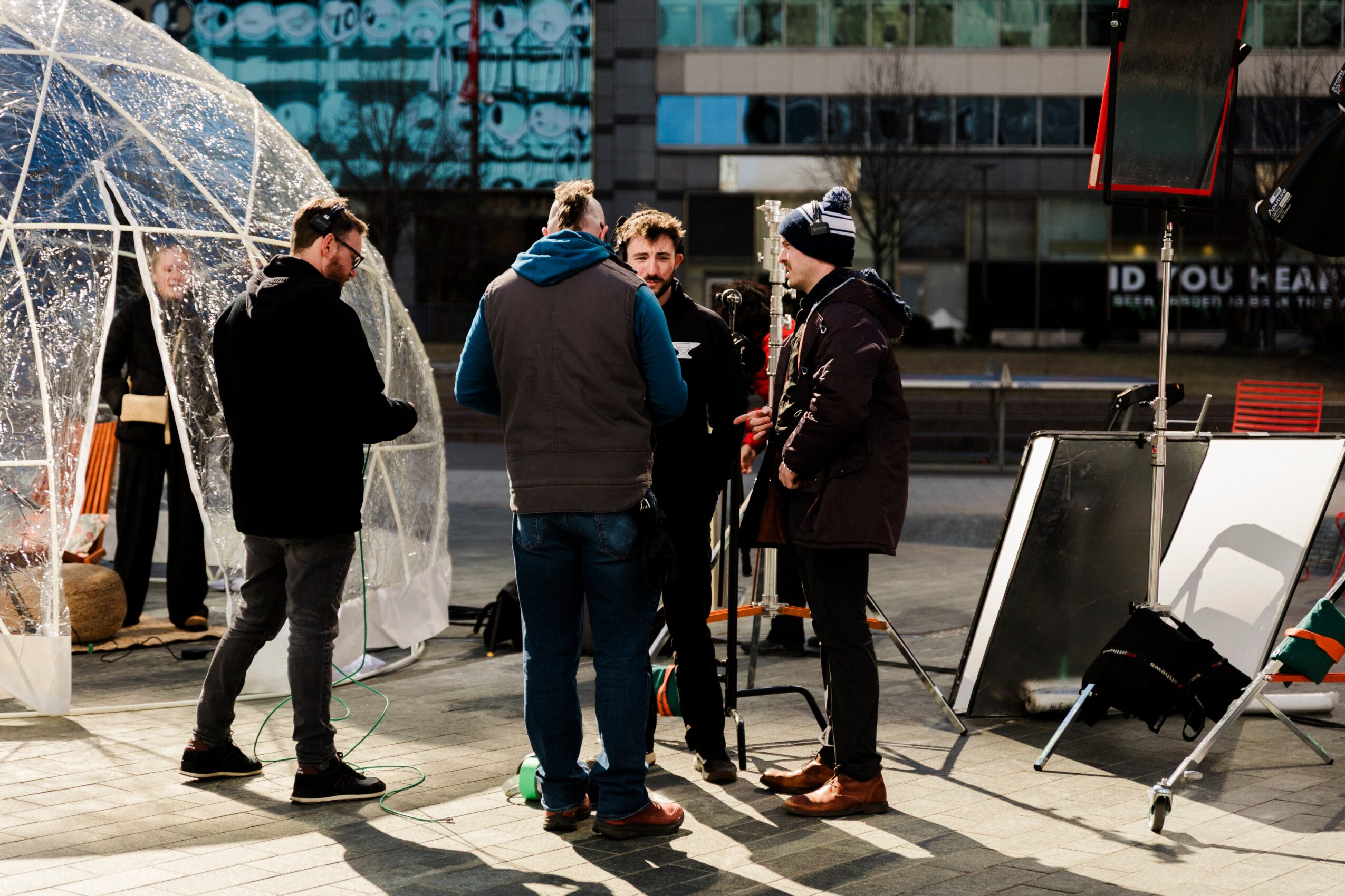 Group of five people standing and talking outdoors near a transparent dome structure, with city buildings in the background.