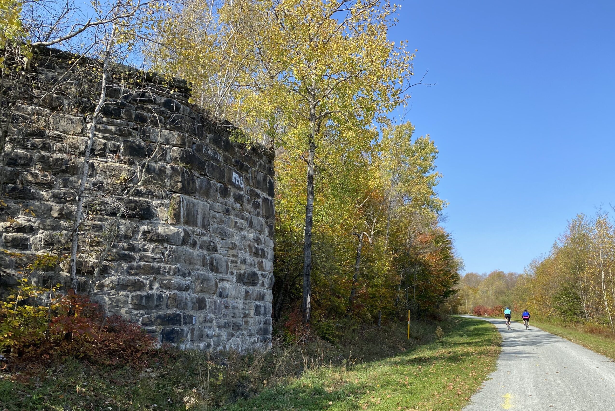 Stone wall on the left with trees and a clear blue sky in the background.