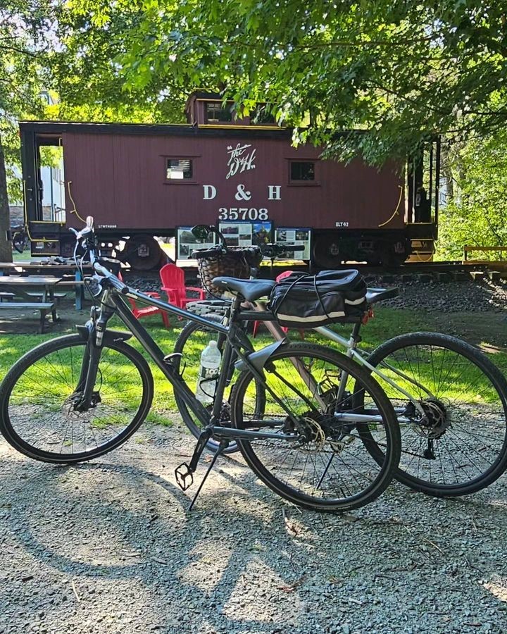 Two bicycles parked on a gravel path with a train car and green trees in the background.