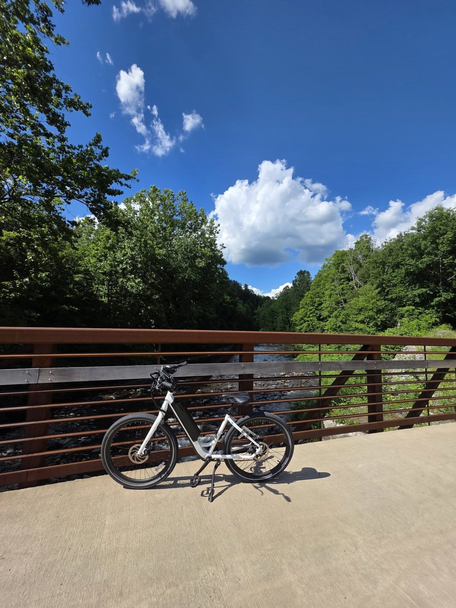 Bicycle parked on a bridge with a river, trees, and a blue sky with clouds in the background.
