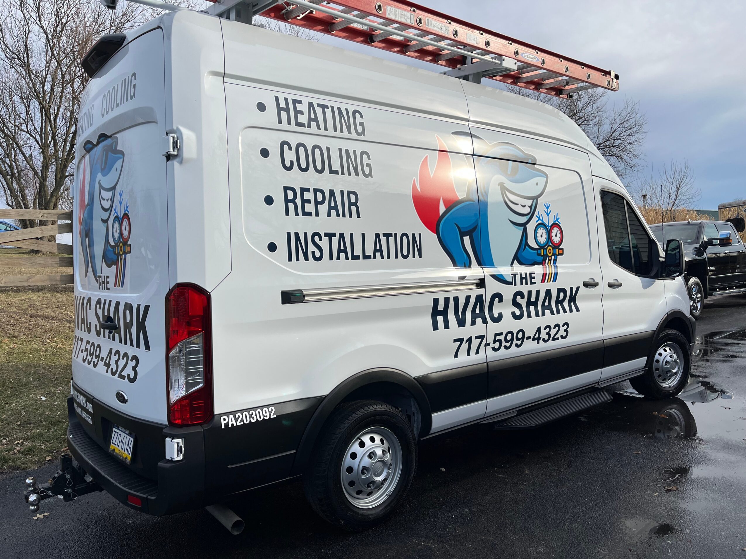 Side view of a white HVAC service van with shark logo and list of services, parked outdoors on wet pavement.