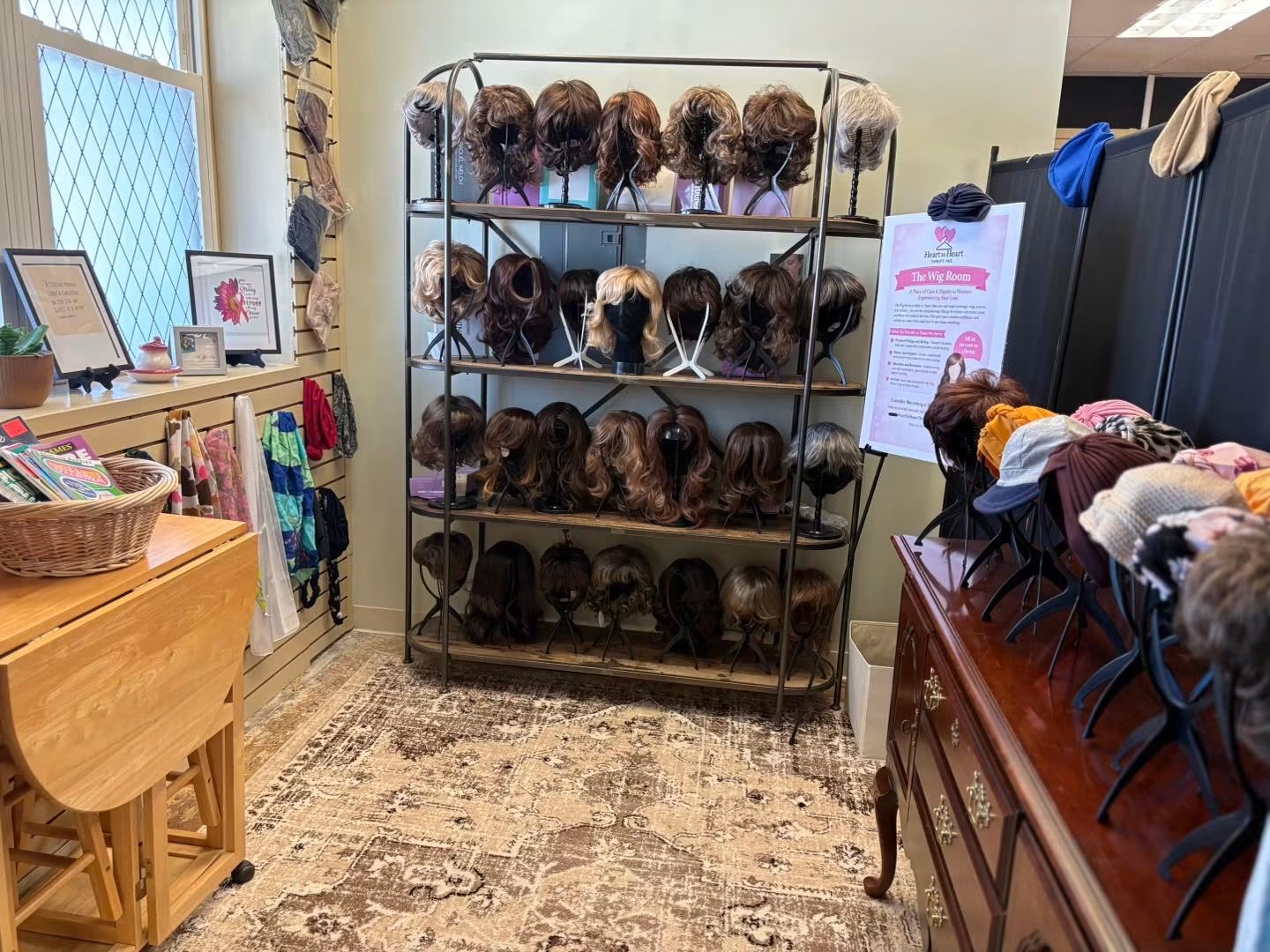 Display of various wigs on a metal rack in a room with wooden furniture and a window.