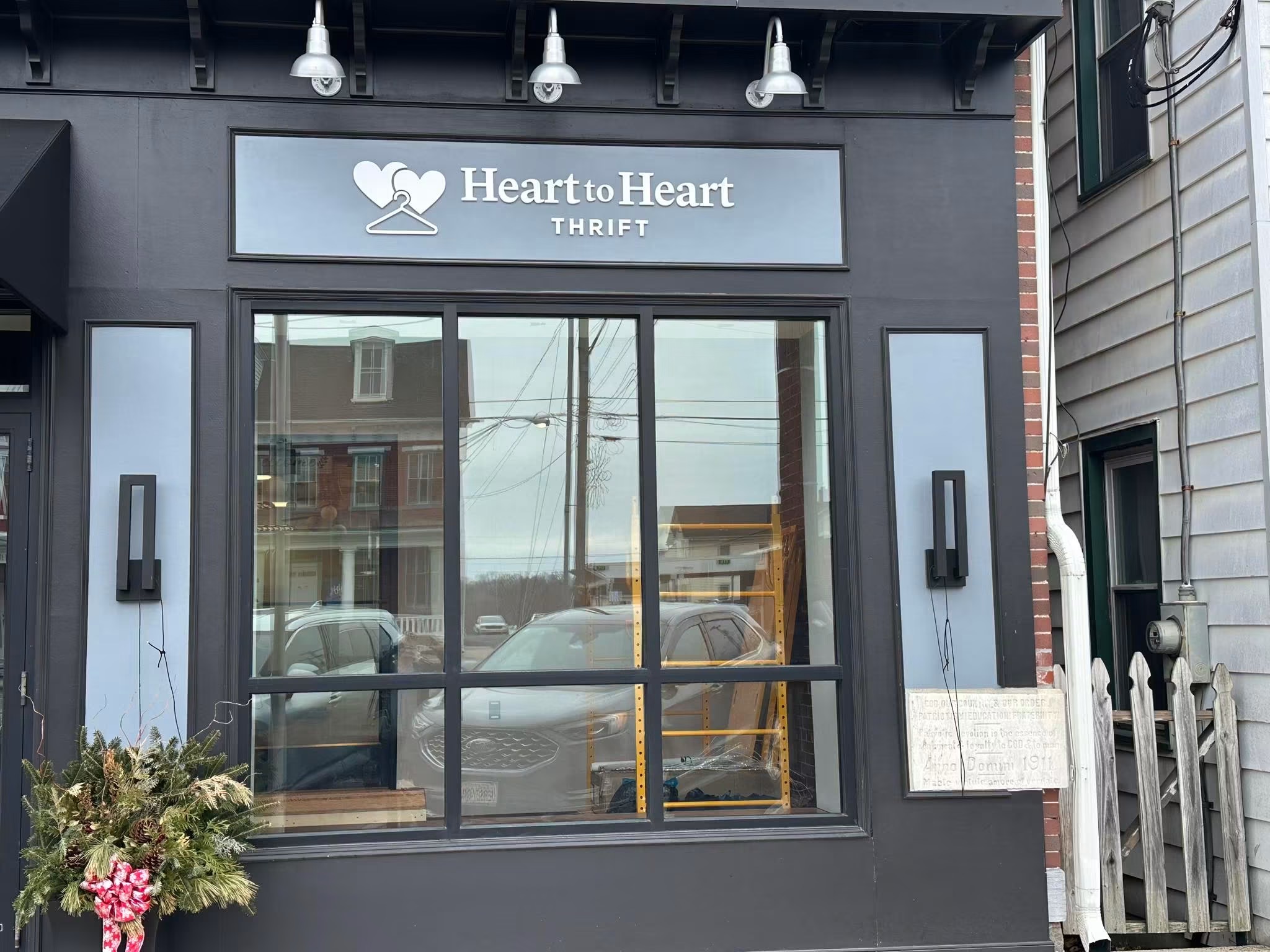 Storefront with a sign reading 'Heart to Heart Thrift' and large window reflecting street scene.