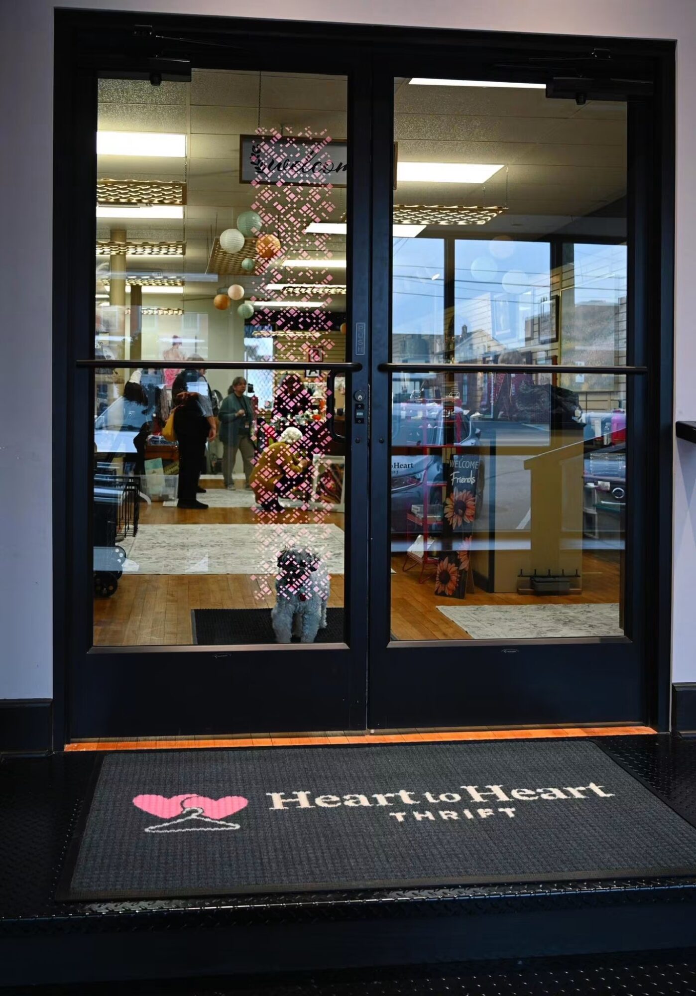 Glass door with Heart to Heart logo mat outside, view of decorated interior with balloons and people inside.