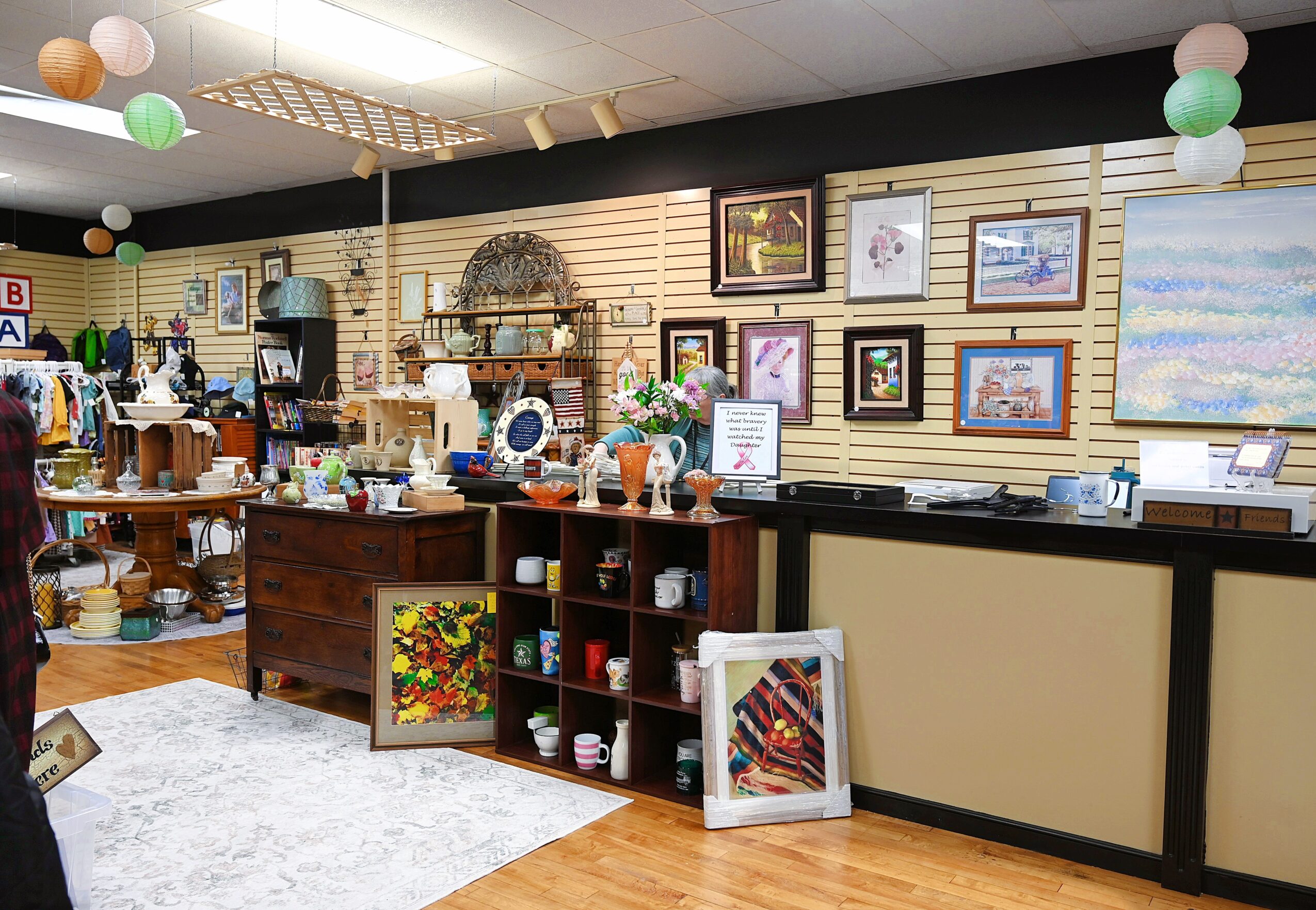Interior of a store with shelves, framed pictures, and various items on display, including ceramics and artwork.