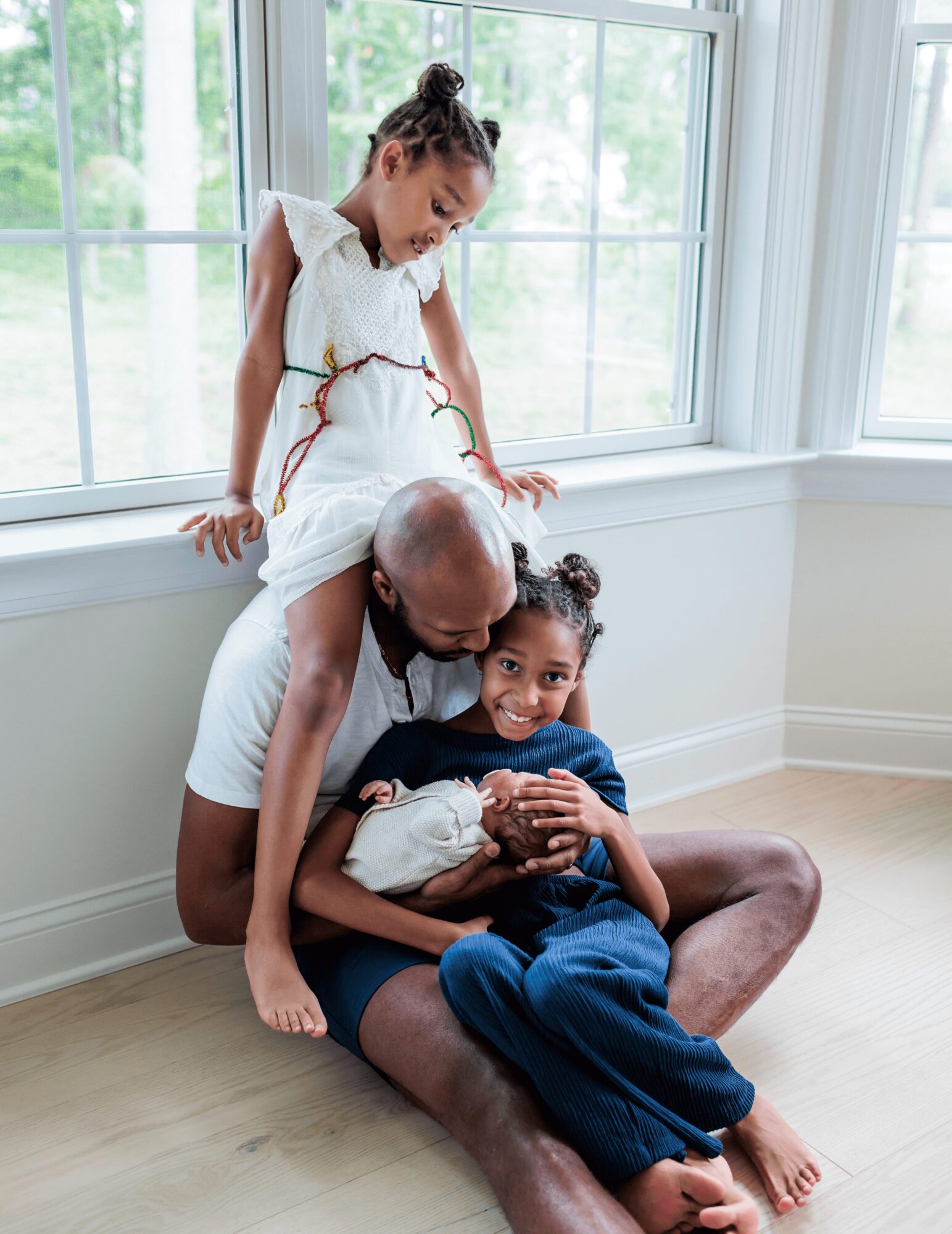A man and two children sitting by a window, smiling and playing together indoors.
