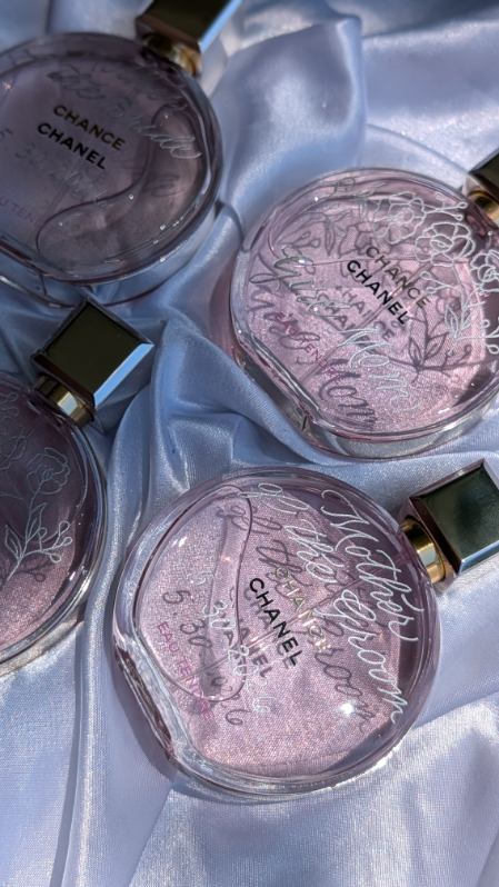 Three Chanel perfume bottles and a small black box on light blue satin fabric, with pink and purple liquid inside bottles.
