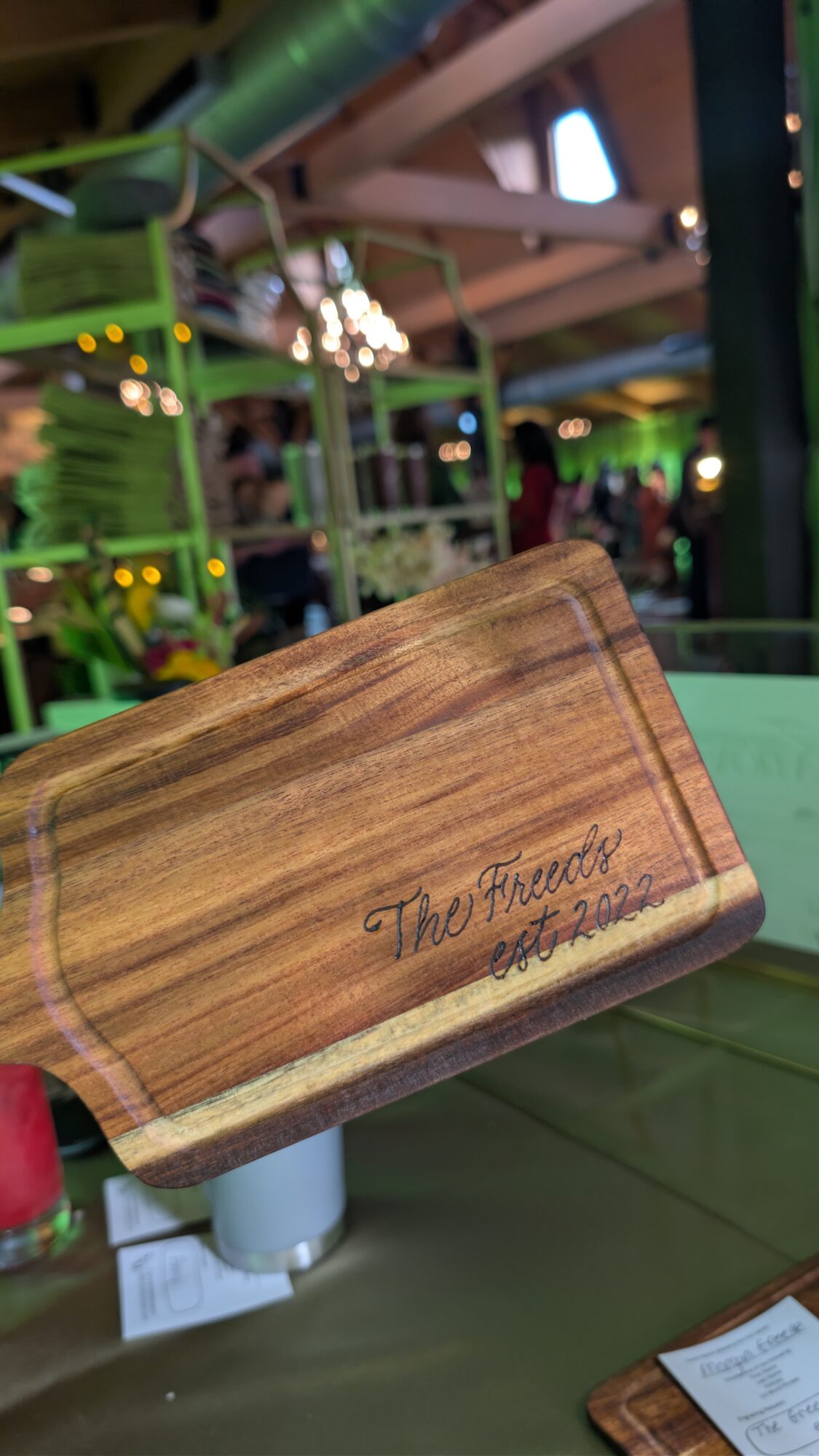 Wooden sign with engraved text, partially visible, in an indoor setting with green and yellow decor, blurred background.