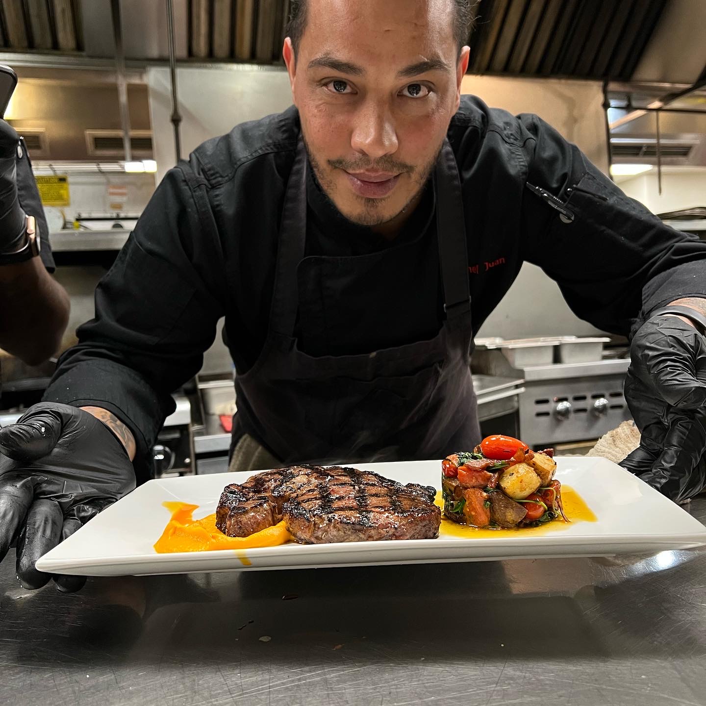 Chef presenting a plated steak with vegetables on a white dish in a professional kitchen.