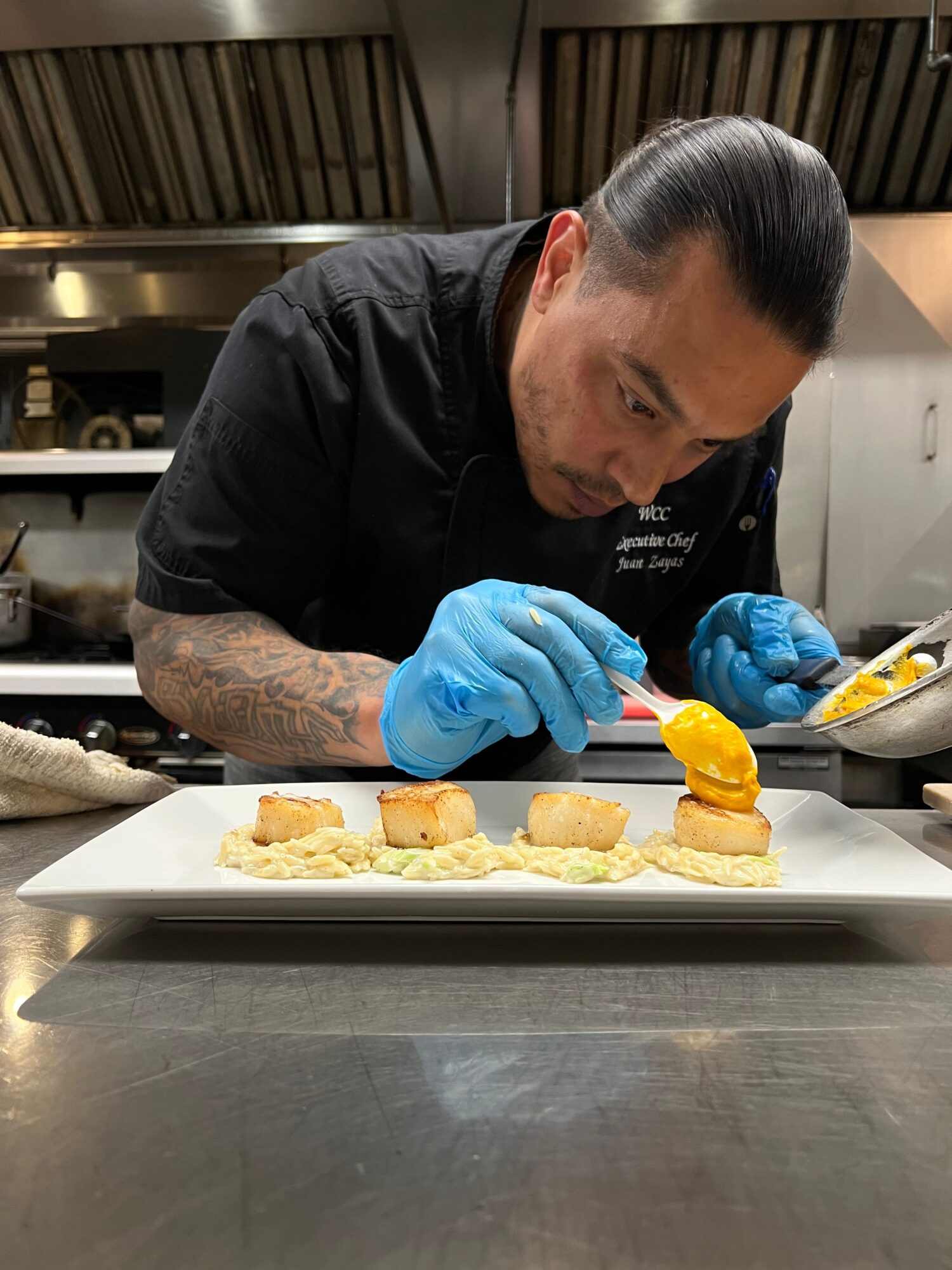 Chef decorating a dessert with orange slices on a white plate in a professional kitchen.