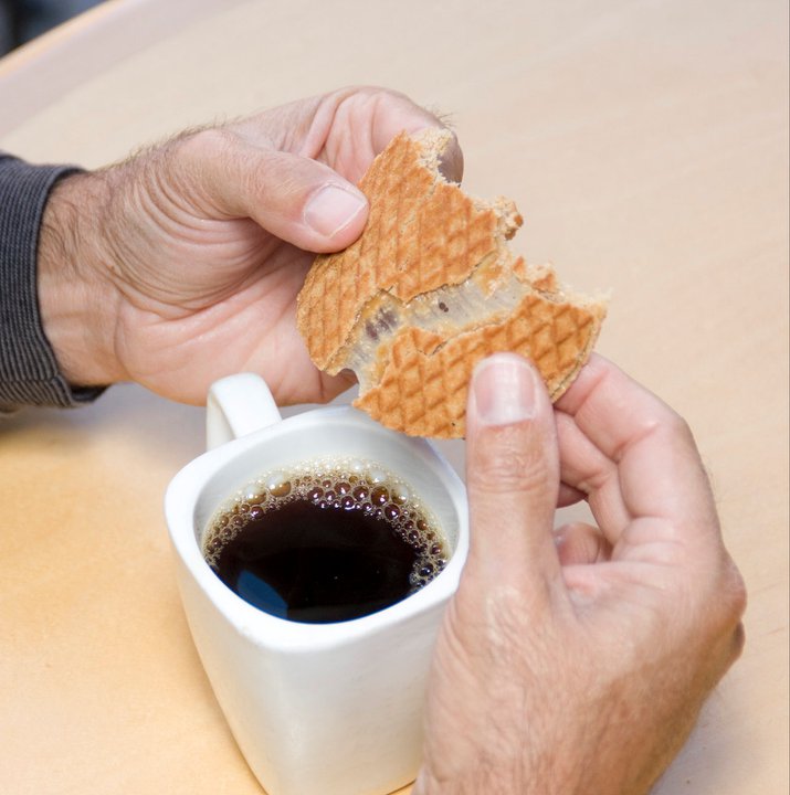 Person holding a waffle and a cup of coffee on a light-colored surface.