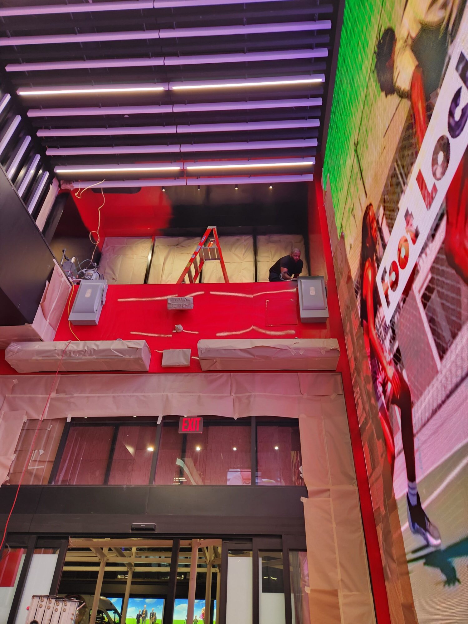 Indoor space with red tables, chairs, and a wall with vertical purple and white lights, viewed from the side.