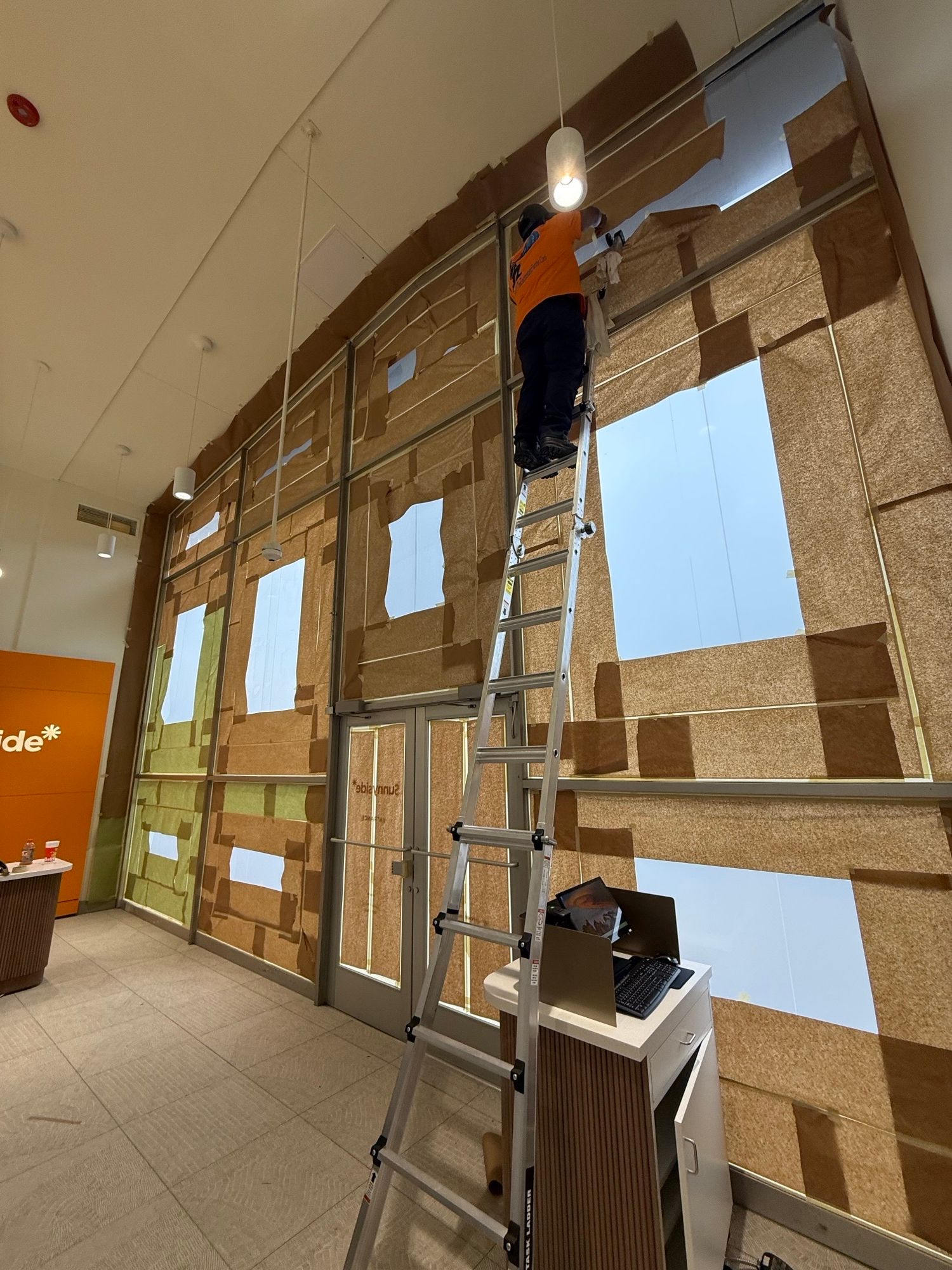 Construction worker on a ladder installing a large window in a building under construction.