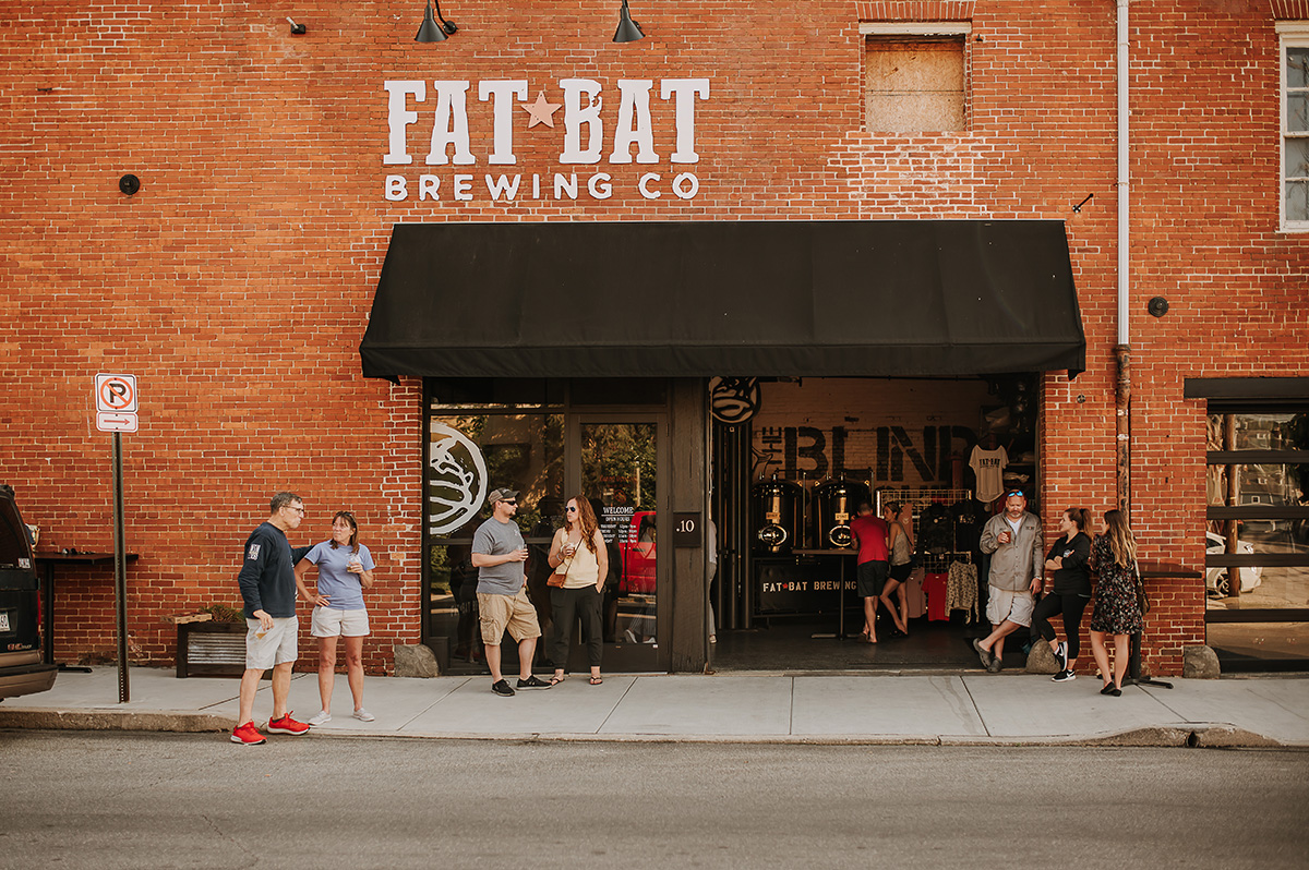 People stand outside a brick building with a black awning, the sign reads 'FAT BAT BREWING CO'.