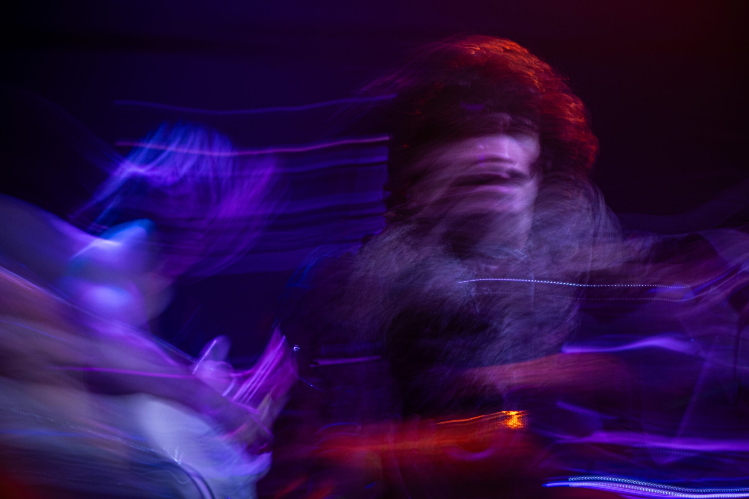 Blurred image of a person with red hair in a dark setting with colorful light streaks.