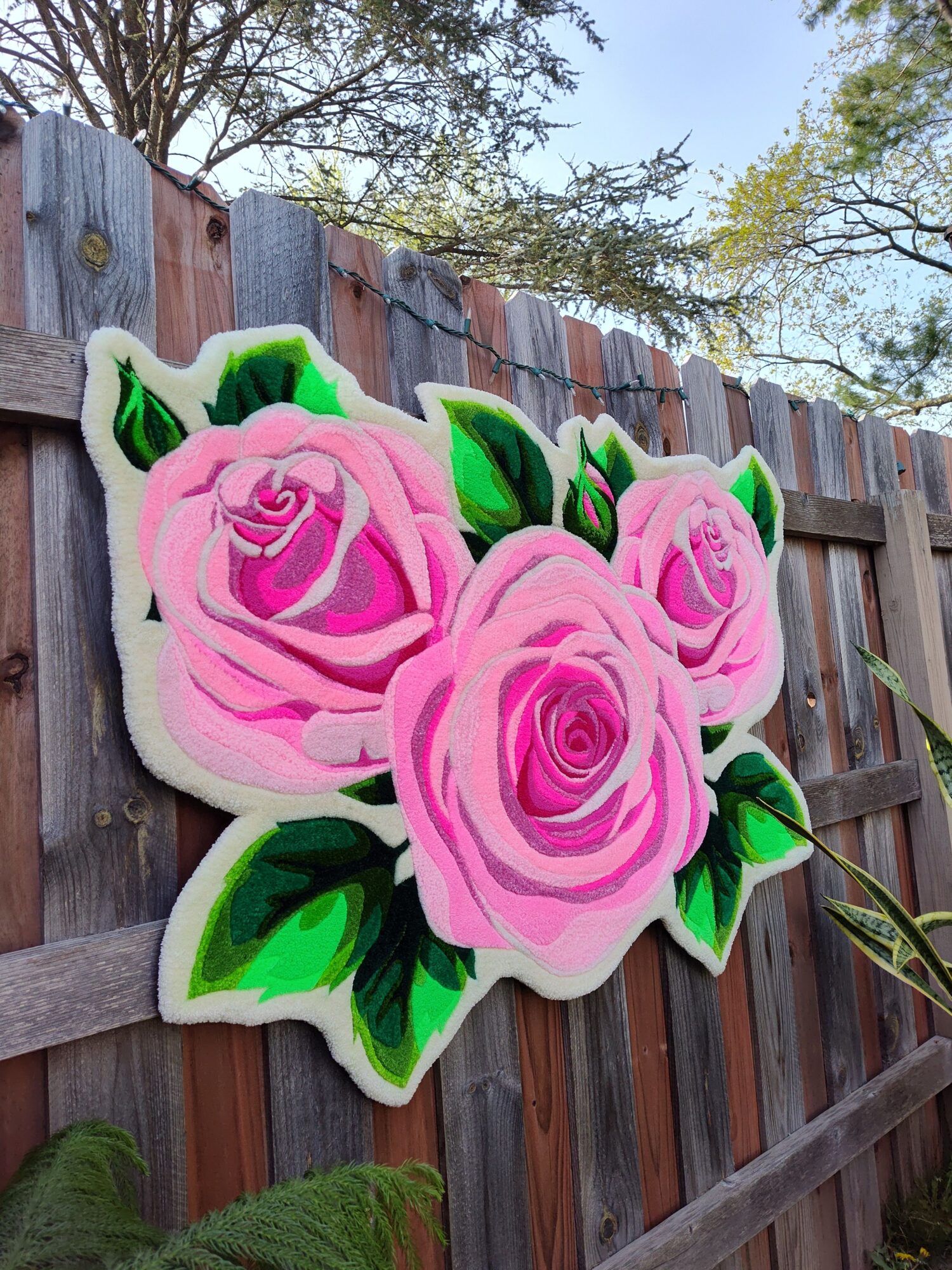 Decorative pink roses with green leaves on a wooden surface outdoors.