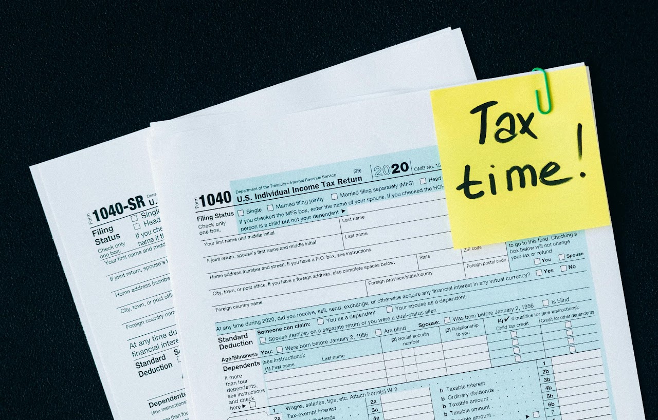Tax documents with a yellow sticky note reading 'Tax time!' on a black background.