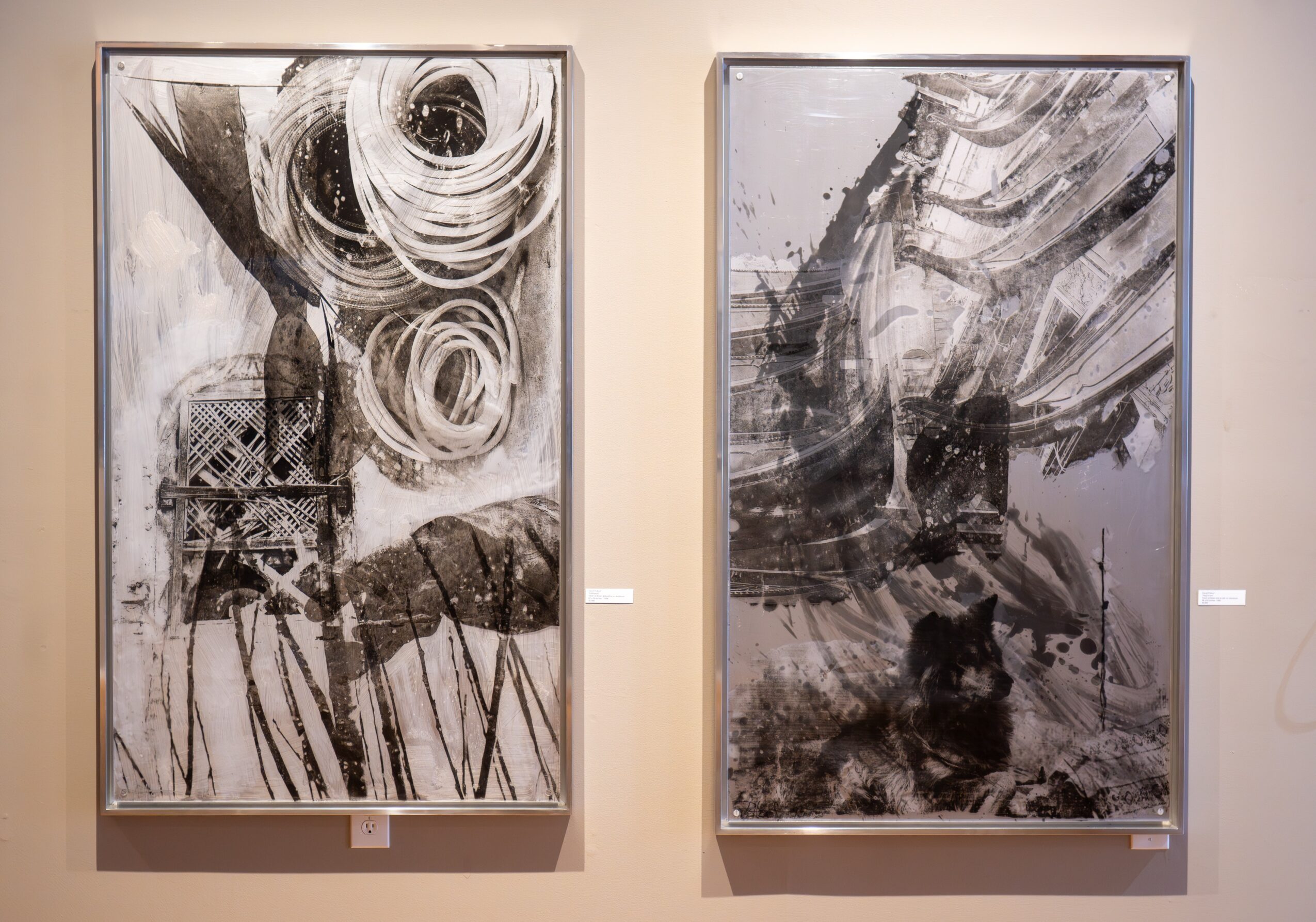 Two abstract black and white paintings on a beige wall, with swirling and dynamic brushstrokes.