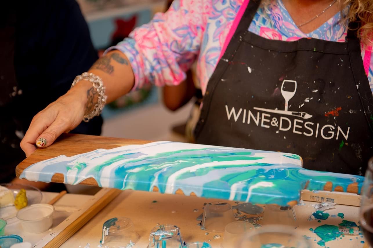 Person wearing an apron with wine glass logo, working on a colorful cake with blue and white marbled icing, in a kitchen.
