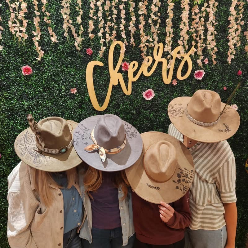 Four children wearing hats stand in front of a floral backdrop with a sign that says 'Cheers'.