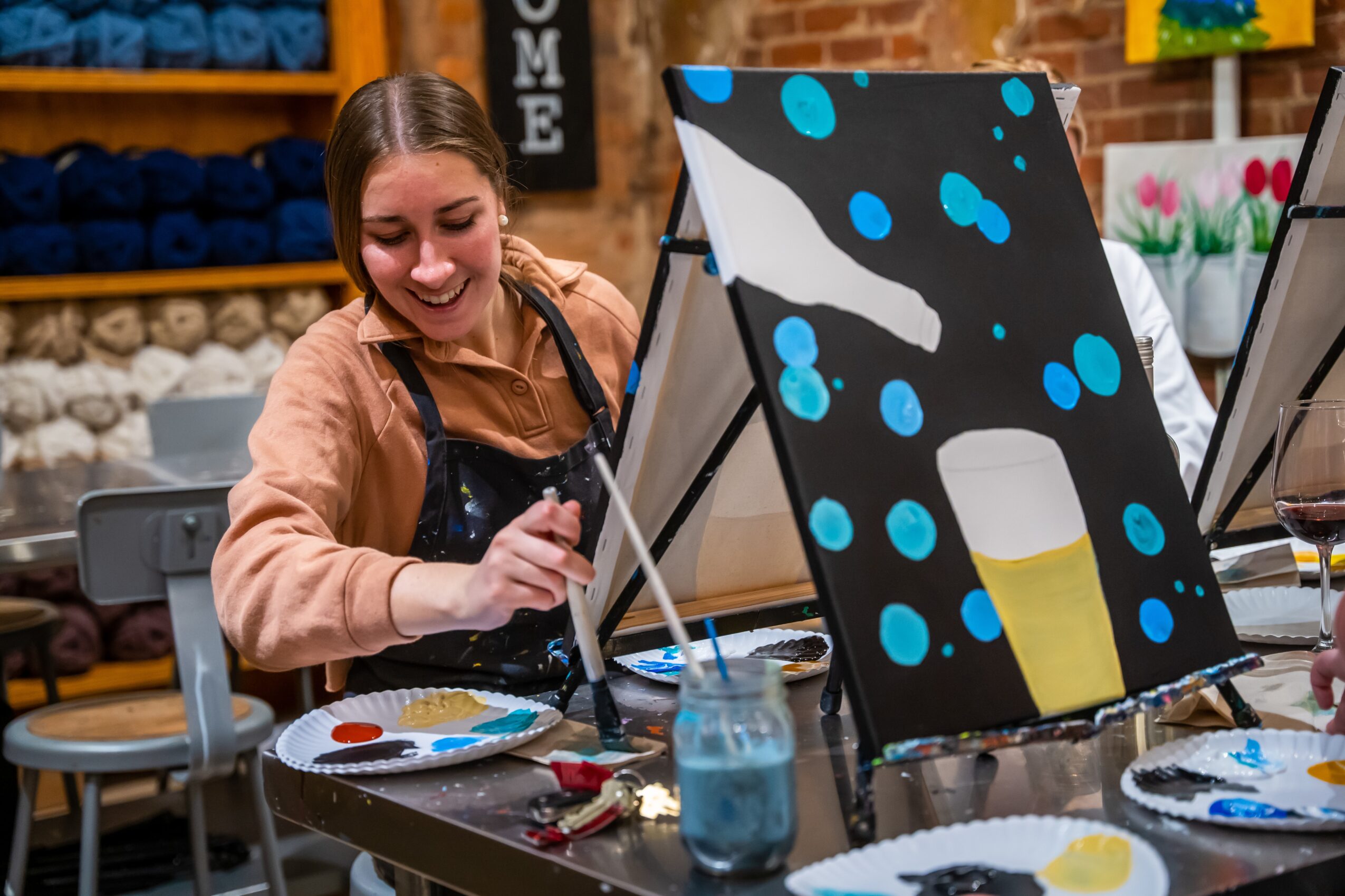 Young woman smiling while painting an abstract canvas with blue, white, and yellow colors in a studio.