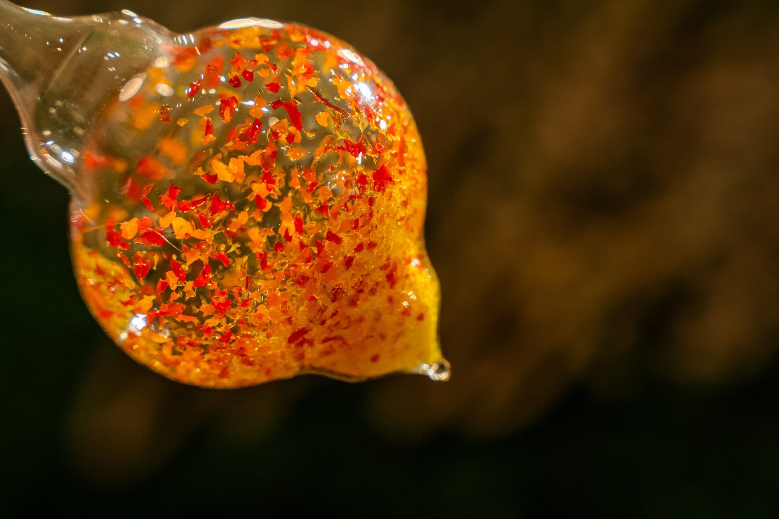 A close-up of a yellow-orange object with red speckles, possibly a fruit or a decorative item, against a dark background.