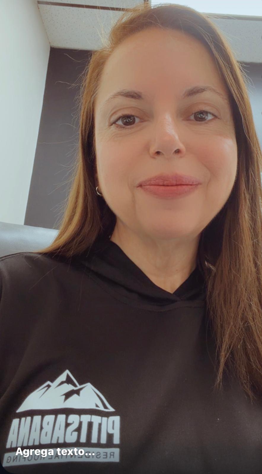 Close-up of a woman with long brown hair smiling, wearing a black hoodie with a mountain logo.