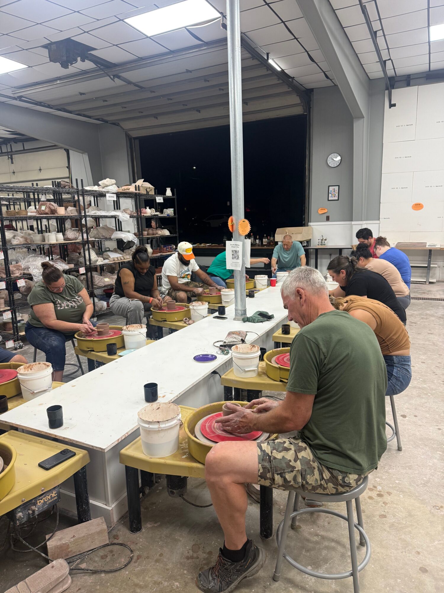 People gathered around a table working on pottery projects in a workshop setting.