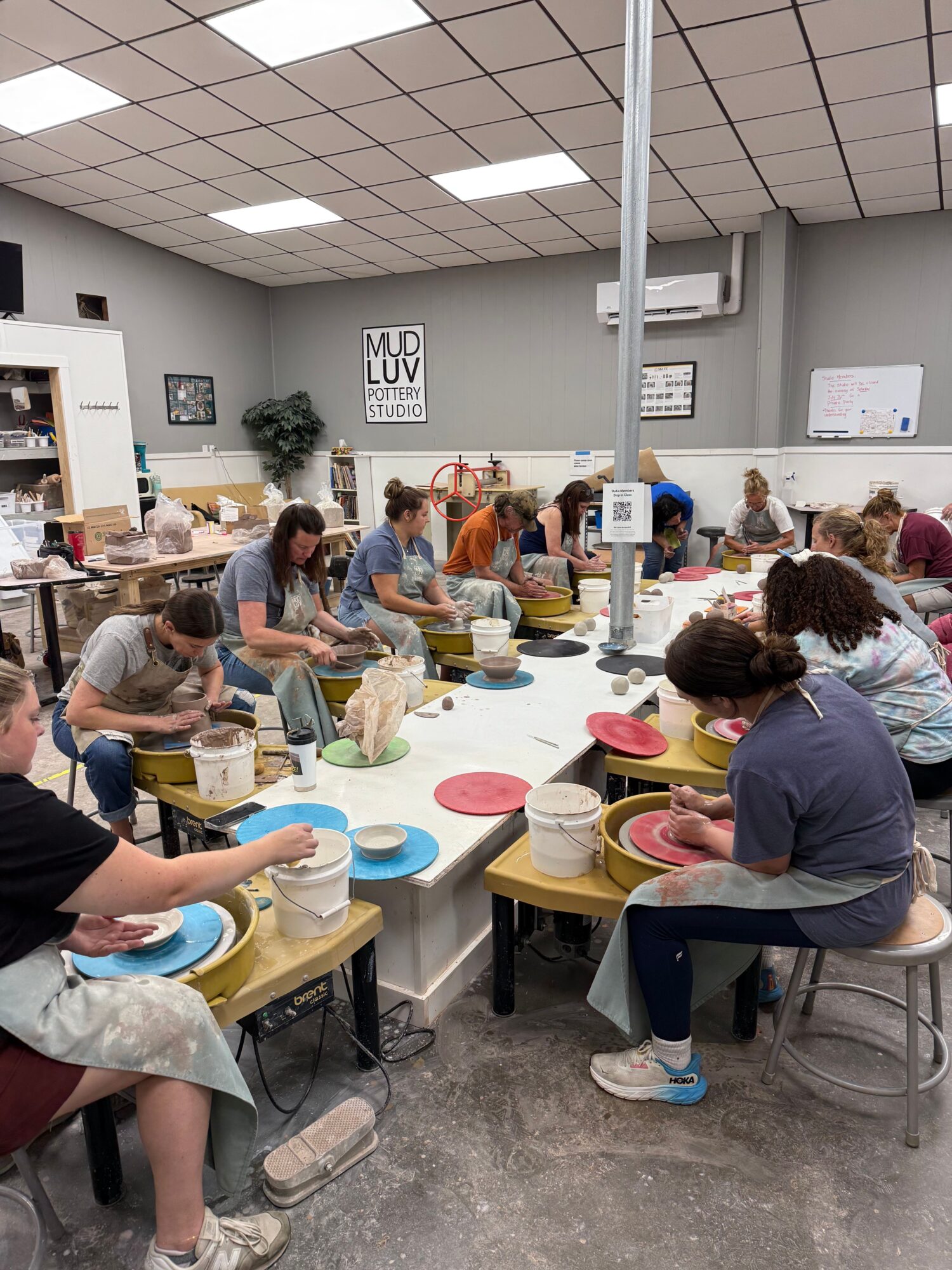 People gathered around tables with colorful plates, serving food in a room with tiled walls and ceiling lights.