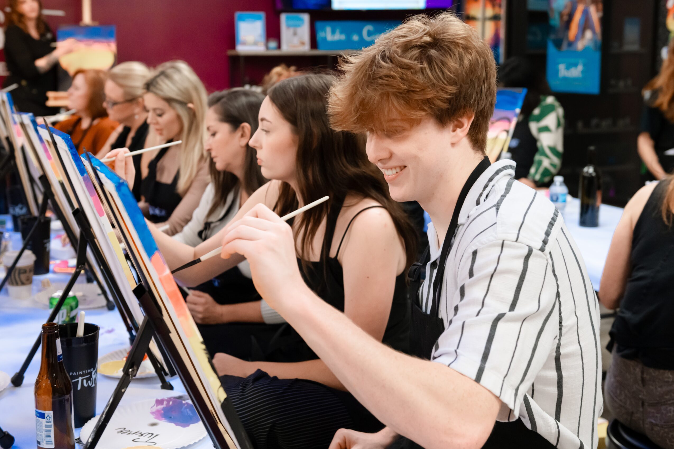 Group of young people painting on canvases at an art event, smiling and focused.