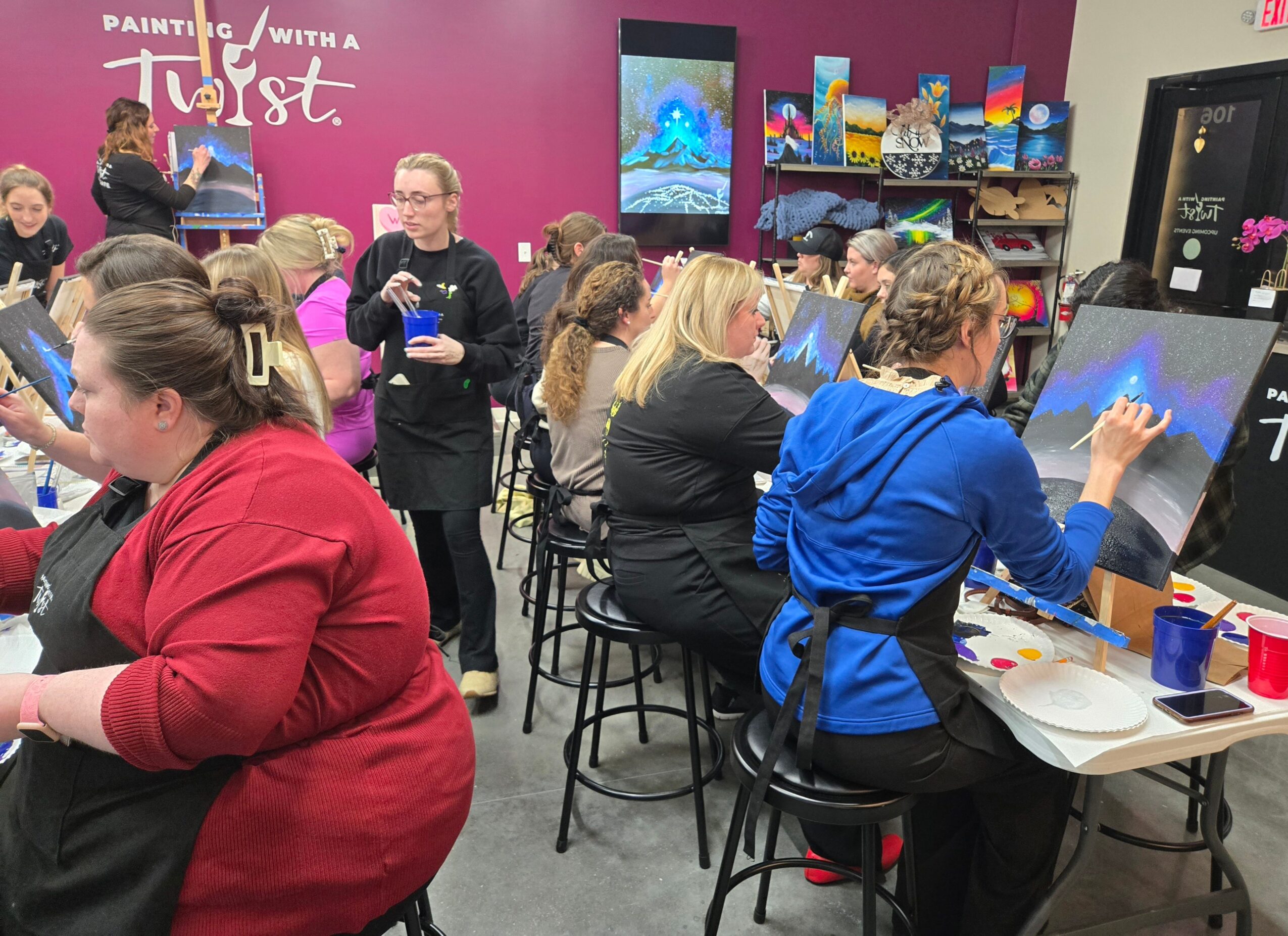 People, mostly women, using touchscreen painting stations in a colorful art store or workshop space.