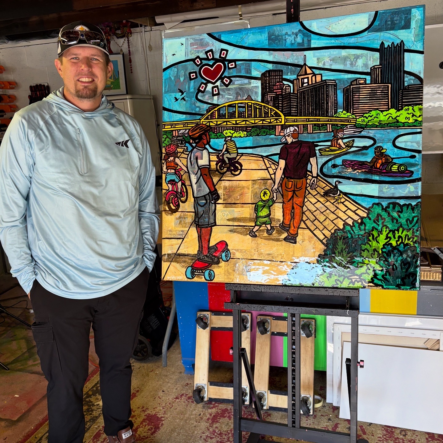 Man standing next to a colorful cityscape painting with people, a bridge, and water, indoors. Bright colors and detailed scene.