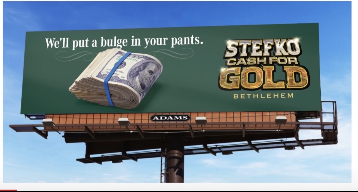 Billboard with a stack of money and text about cash for gold, against a blue sky background.