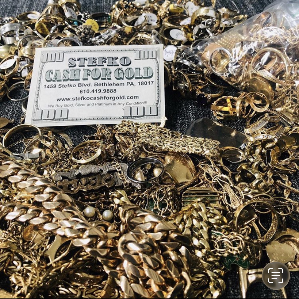 A pile of gold and silver jewelry, including chains, rings, and bracelets, with a business card on top.