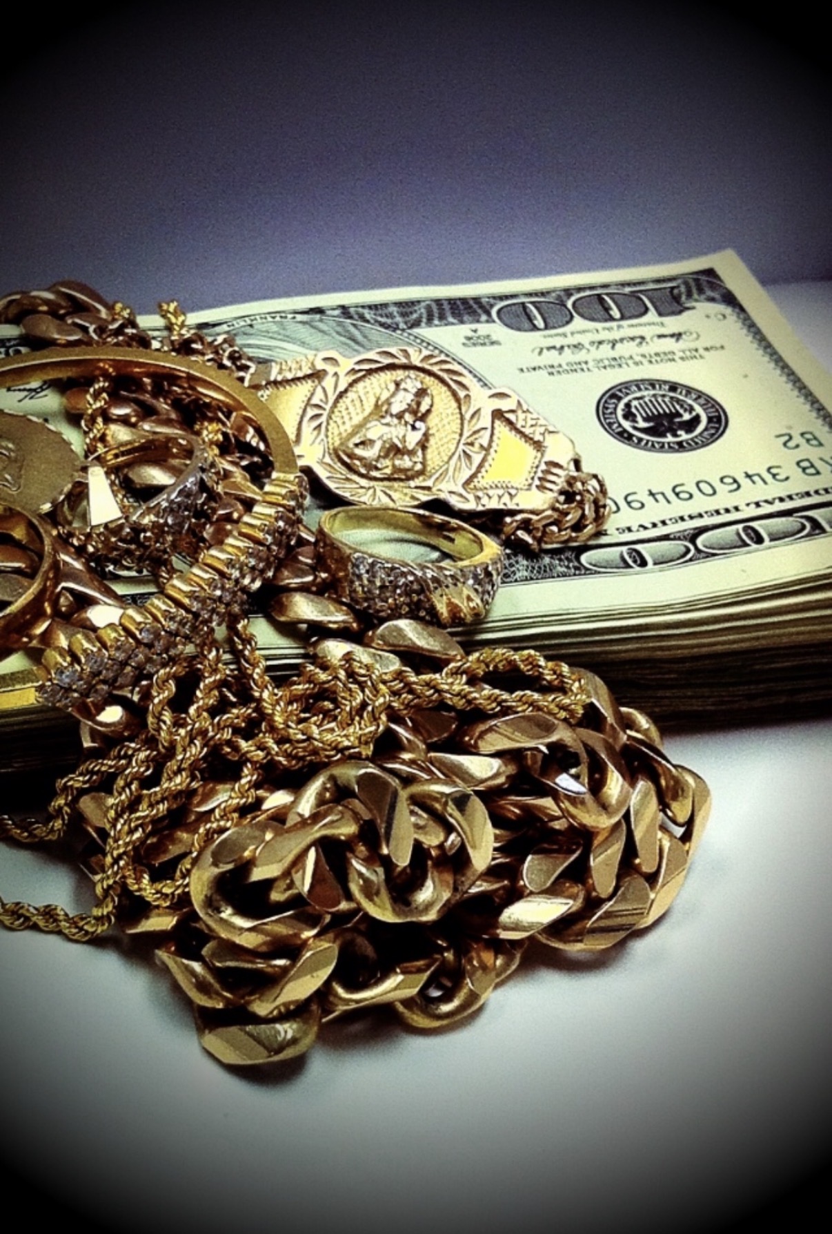 Gold jewelry and watches placed on a stack of hundred-dollar bills, with a dark background.
