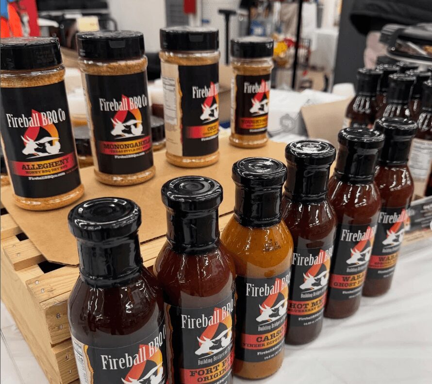 Assorted bottles of barbecue sauce on a table, with a background of store shelves and other products.