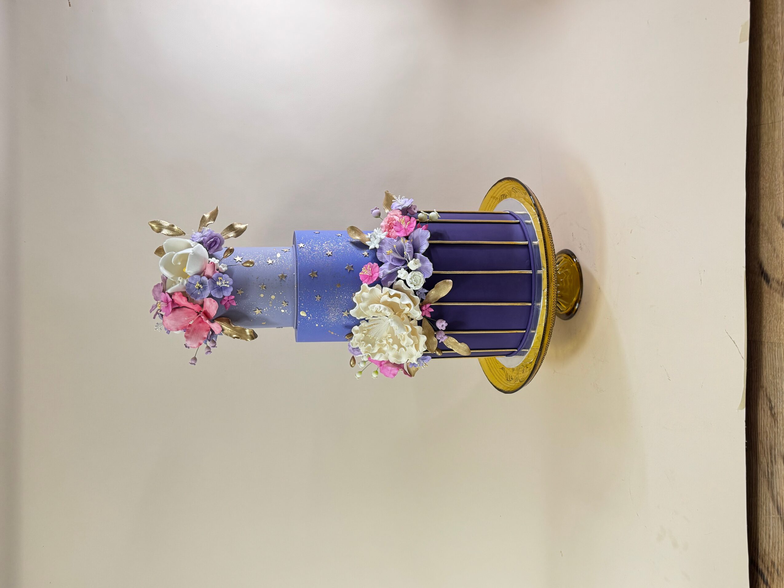 Decorative flower arrangement in a blue and purple container with flowers, on a white surface.