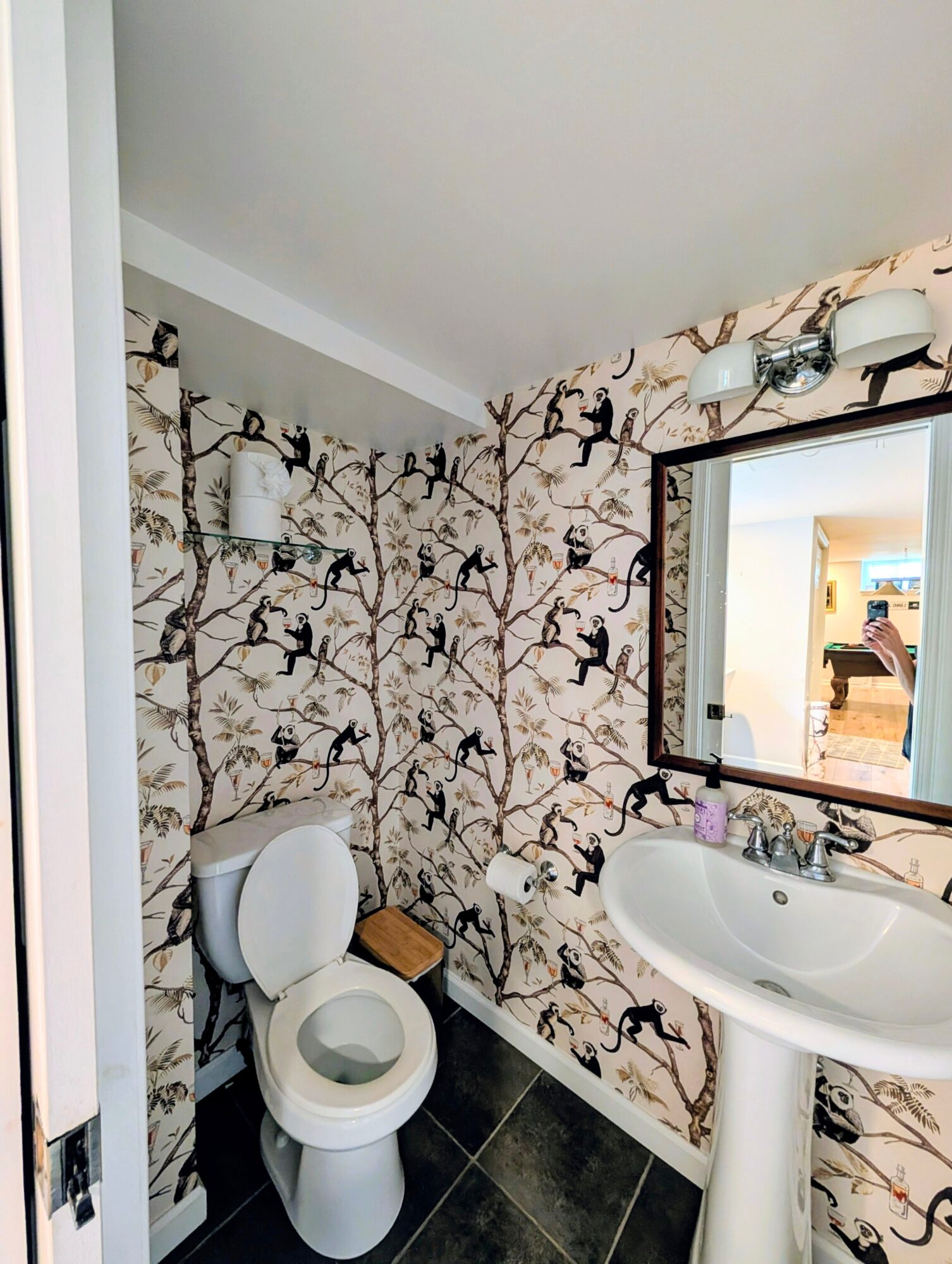 Bathroom with patterned wallpaper, toilet, and sink, mirror above sink, and light fixture, viewed from doorway.