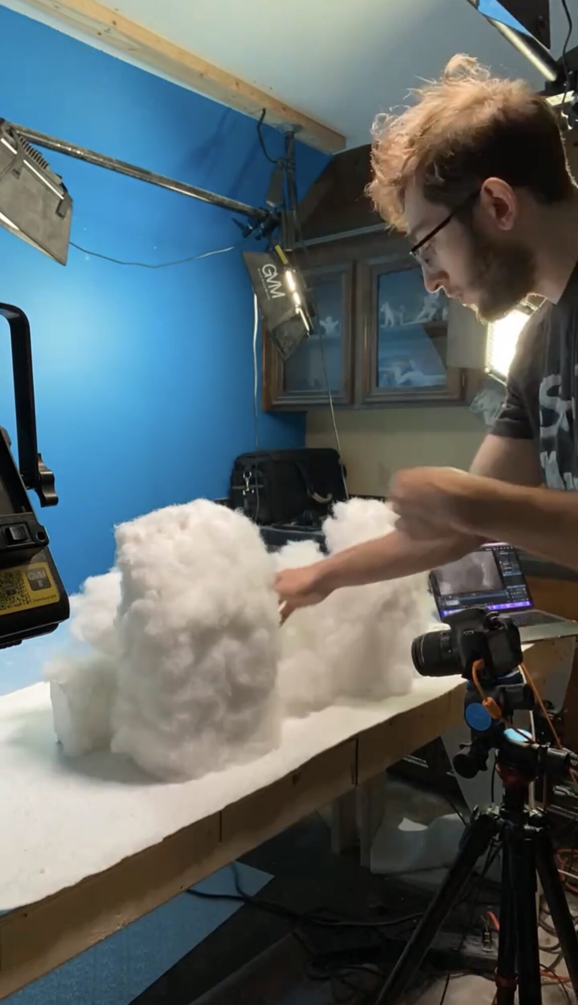 Person working with cotton-like material in a room with blue walls and windows, using equipment on a table.